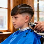 Garçon aux cheveux lisses recevant une coupe dégradé moderne dans un salon de coiffure avec cape bleue