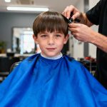Jeune garçon aux cheveux lisses portant une cape bleue vif pendant sa coupe chez le coiffeur
