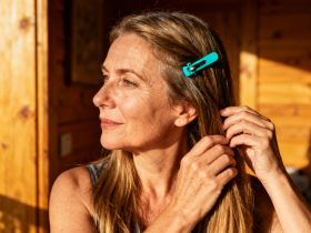 Femme européenne de 55 ans touchant délicatement ses longs cheveux sains, ornés d'un clip turquoise vibrant
