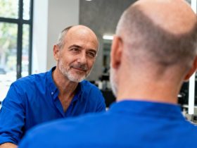 Homme de 55 ans avec calvitie vertex en chemise bleue en consultation chez le coiffeur, regardant le miroir