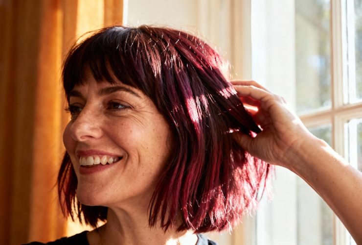 Femme souriante de 35 ans avec une coupe à étages et reflets bordeaux, jouant avec ses cheveux dans une lumière naturelle